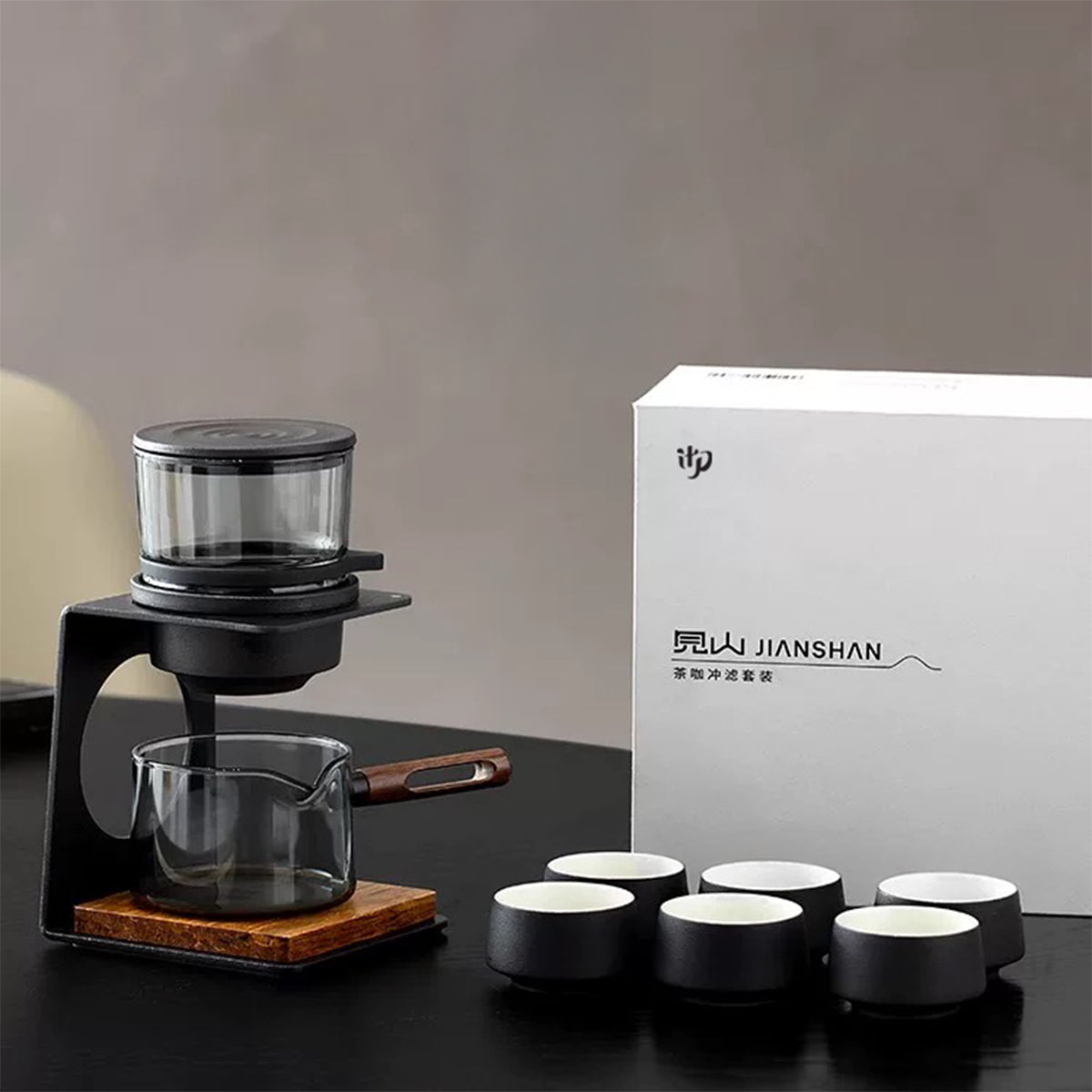 Tea-making set with black and wooden components and a white box labeled 'JIANSHAN' on a dark surface.